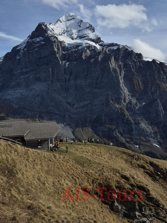 Великолепный горный пейзаж с заснеженной вершиной и группой людей, наслаждающихся видом. Spectacular mountain landscape featuring a snow-capped peak and a group of people enjoying the view.