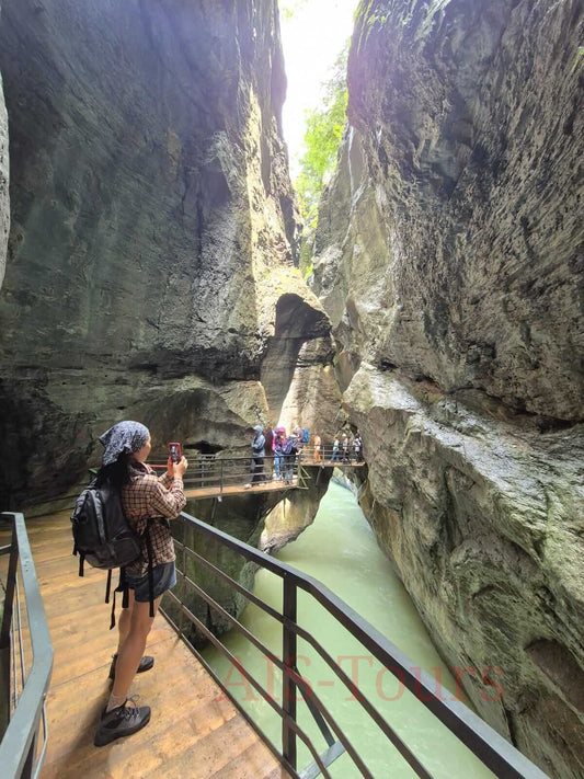 Турист фотографирует живописное ущелье со скалистыми стенами и спокойной рекой внизу. Hiker taking photos in a picturesque gorge with rocky walls and a calm river below.